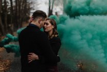 Pareja joven besándose en el bosque por nube de humo verde - foto de stock