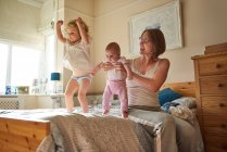Woman on bed playing with baby and toddler daughters — Stock Photo