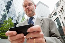 Businessman using smartphone with office buildings at background — Stock Photo