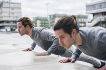 Young male twins doing push ups against wall in city — Stock Photo