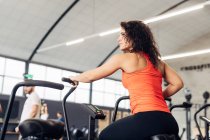 Visão traseira da mulher em bicicleta de exercício no ginásio — Fotografia de Stock