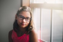Портрет молодой девушки в очках, стоящей у окна — стоковое фото