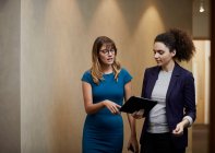 Businesswomen walking and looking at digital tablet in office corridor — Stock Photo