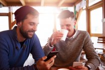 Junge Männer lächeln über SMS auf Mobiltelefonen — Stockfoto