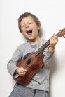 Мальчик играет на укулеле на белом фоне — стоковое фото