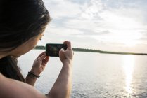 Vista posteriore di Giovane turista femminile fare foto con smartphone di Chobe River, Botswana, Africa — Foto stock