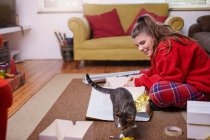 Young woman sitting on living room floor wrapping gifts and watching cat — Stock Photo