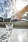 Frau gießt Wasser aus durchsichtiger Karaffe in Glas — Stockfoto