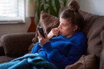 Молодая женщина на диване смотрит на смартфон — стоковое фото