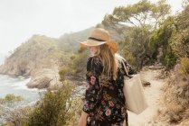 Cappello donna in cappello da sole passeggiando lungo il sentiero costiero — Foto stock