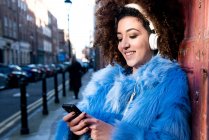 Portrait of woman in street listening music through headphones on smartphone — Stock Photo