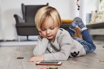 Niño tendido en el suelo y mirando en el teléfono inteligente - foto de stock