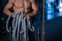 Hombre ejercitándose en el gimnasio, sosteniendo la cuerda, preparándose para el entrenamiento en trineo, sección media - foto de stock