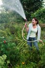 Sorrindo mulher pulverizando jardim com mangueira — Fotografia de Stock
