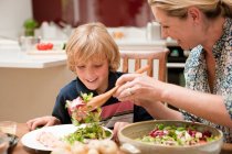Мать подает салат сыну за обеденным столом — стоковое фото