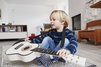 Jovem sentado com guitarra em torno do pescoço — Fotografia de Stock