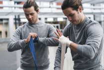 Boxeadores gemelos vendando manos con envolturas de mano - foto de stock