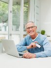 Senior man using laptop with credit card — Stock Photo