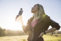 Jeune femme tenant une bouteille d'eau et faisant de l'exercice à l'extérieur — Photo de stock