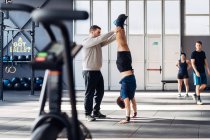 Man in gym helping friend do handstand — Stock Photo