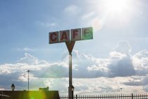 Cafe sign against sky with clouds with lens flares — Stock Photo