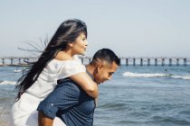 Man giving woman piggyback along beach, Seal Beach, California, USA — Stock Photo