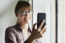 Frau mit Brille blickt aufs Smartphone und lächelt — Stockfoto