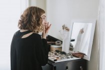 Vista lateral da mulher na mesa de vestir aplicando maquiagem — Fotografia de Stock