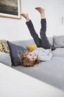 Jovem deitada no sofá com as pernas no ar — Fotografia de Stock