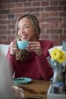 Mulher sorridente bebendo café sentado no café — Fotografia de Stock