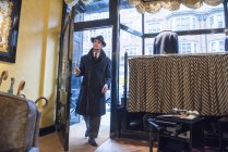 Male customer in winter coat and trilby arriving in tailors shop — Stock Photo