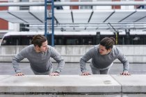 Jóvenes gemelos haciendo flexiones contra la pared en la ciudad - foto de stock