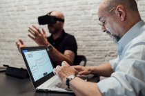 Колеги, що працюють з гарнітурою віртуальної реальності та ноутбуком — стокове фото