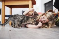 Молода дівчина грає з котом на підлозі — стокове фото