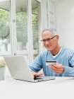 Старший чоловік використовує ноутбук з кредитною карткою — стокове фото