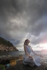 Женщина, сидящая на скалах по морю и медитирующая, Пальма де Майорка, Ислас Балеарес, Испания, Европа — стоковое фото