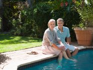Зрелая пара, сидящая у бассейна в саду — стоковое фото