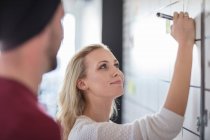 Male and female colleague planning  ideas on office whiteboard, over shoulder view — Stock Photo