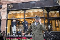Male customer in coat and trilby outside tailors shop — Stock Photo