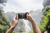 Young female tourist taking smartphone photographs of Victoria Falls, detail of hands, Zimbabwe, Africa — Stock Photo