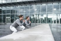 Young male twins training squatting by wall in city — Stock Photo
