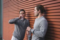 Jovens gêmeos do sexo masculino fazendo pausa de treinamento e bebendo água engarrafada — Fotografia de Stock