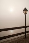 Poste da lâmpada pela cerca de madeira perto do lago nebuloso à noite — Fotografia de Stock