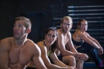 Group of people exercising in gymnasium, catching break after using rowing machines — Stock Photo