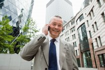 Businessman talking on cellphone and office buildings at background — Stock Photo