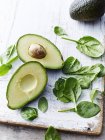 Tagliate a metà le fette di avocado con spinaci baby sul tagliere — Foto stock