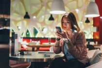 Mujer sentada en restaurante y usando smartphone - foto de stock
