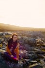 Mujer sentada en las rocas, Fanore, Clare, Irlanda - foto de stock