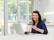 Mature woman using laptop with credit card — Stock Photo