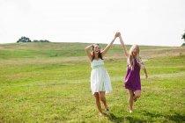 Jovens mulheres pulando através do campo com os braços levantados — Fotografia de Stock